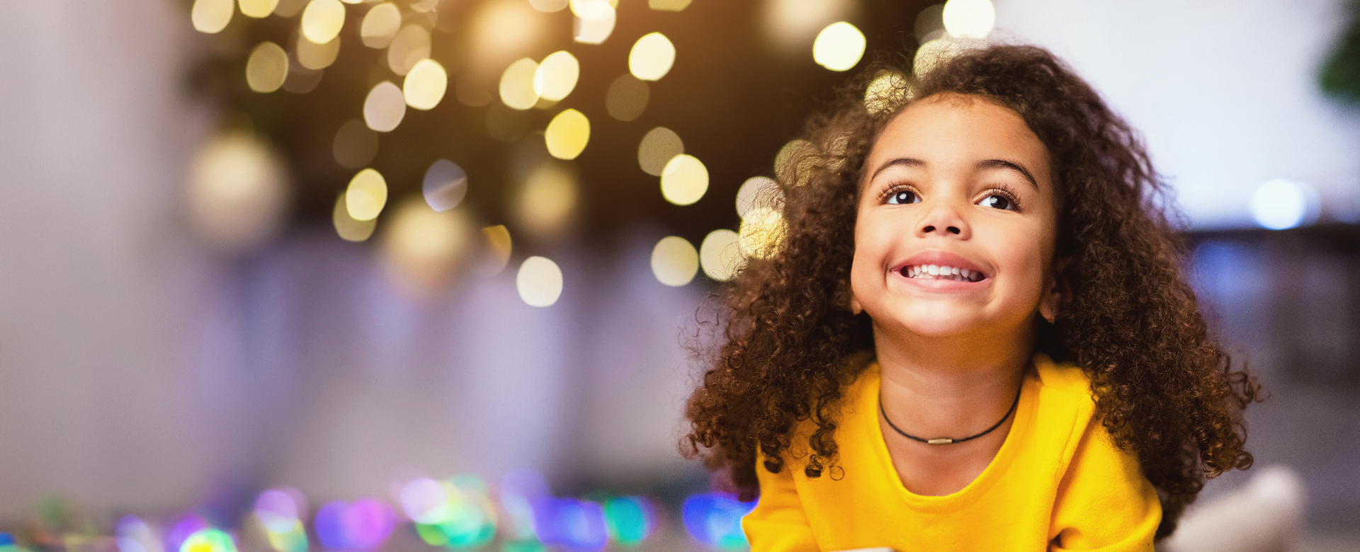 A smiling child gazes upward, surrounded by warm glowing bokeh lights — embodying imagination and possibility.